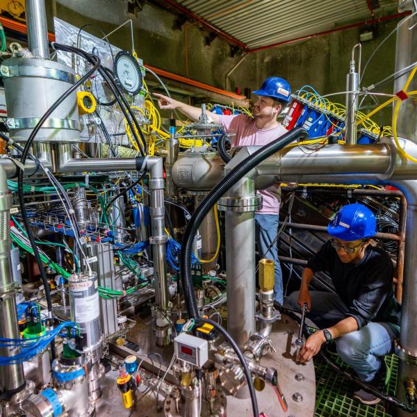 Two people in blue helmets examine experimental equipment.